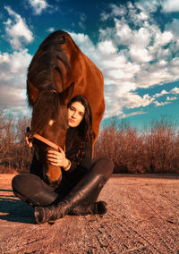 Young woman sitting on field against sky