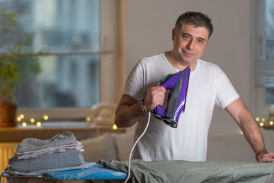 Portrait of smiling mature man ironing cloth at home