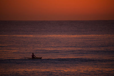 Silhouette man kayaking in sea against sky during sunset