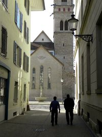 Rear view of people walking on street amidst buildings in city