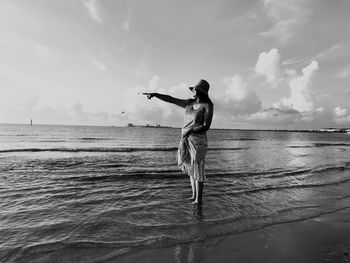 Full length of woman pointing while standing at beach against sky