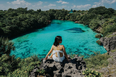 Woman sitting on rock over lake against sky