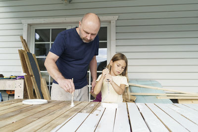 Father and daughter painting planks in back yard