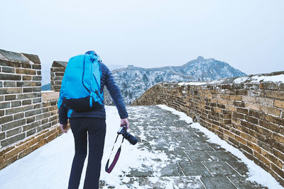 Full length rear view of man walking on snowcapped mountain