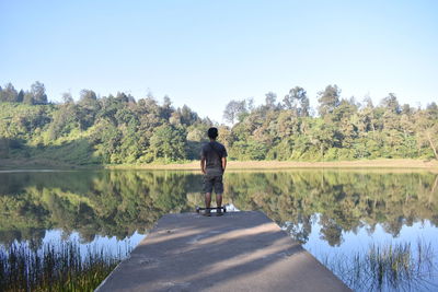 Rear view of man by lake against clear sky
