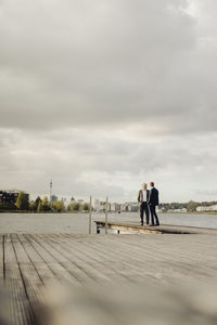 Two businessmen standing on jetty at a lake talking