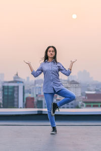 Portrait of young woman doing yoga on building terrace at sunset