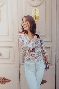 Portrait of a smiling young woman standing against door