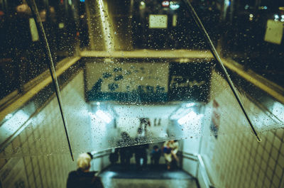 Illuminated subway entrance seen from wet umbrella during rain at night