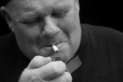 Close-up of man lighting cigarette against black background