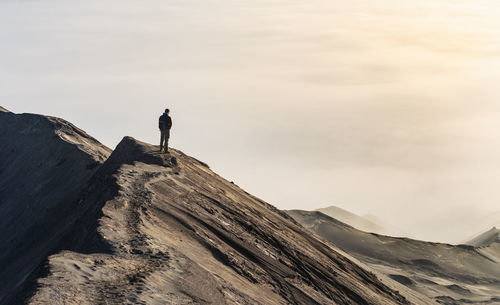 Man standing on rock by mountain against sky