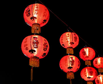 Low angle view of illuminated lanterns hanging against black background