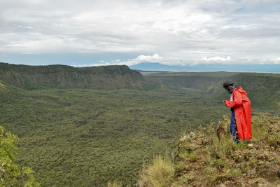 Side view of man wearing red raincoat while standing on mountain against sky