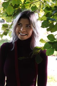 Portrait of smiling young woman standing against tree