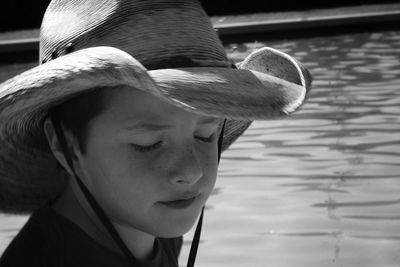 Close-up of boy with closed eyes wearing sun hat against lake