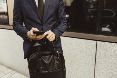 Midsection of entrepreneur surfing net while standing against building