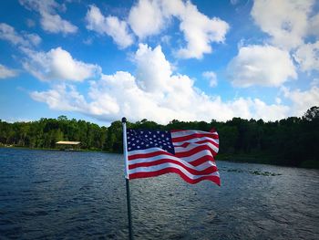 American flag waving over lake against sky