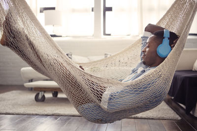 Man listening music while resting on hammock in living room at home