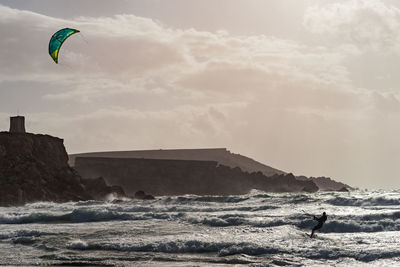 Man kitesurfing in sea against sky