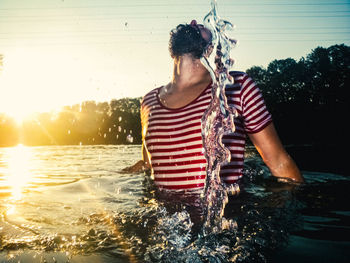 Man splashing water in sea against sky during sunset