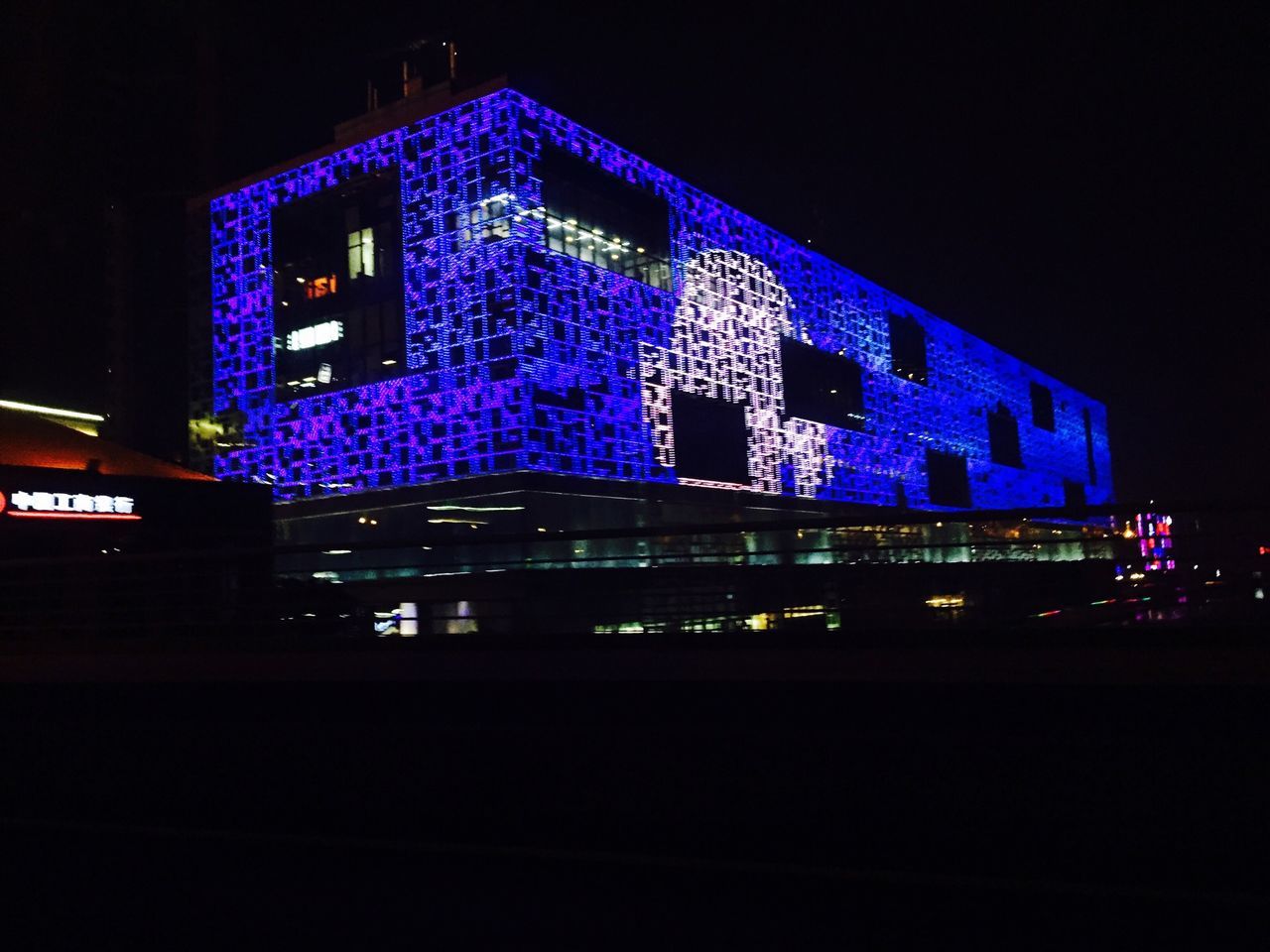 illuminated, night, architecture, built structure, building exterior, text, western script, blue, lighting equipment, city, communication, low angle view, long exposure, dark, light - natural phenomenon, light trail, no people, sky, outdoors, neon