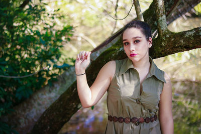 Portrait of young woman holding hair while standing by tree in forest