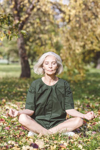 Mature woman doing meditation while sitting at park