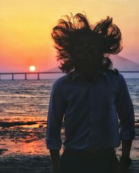 Rear view of young woman standing at beach during sunset