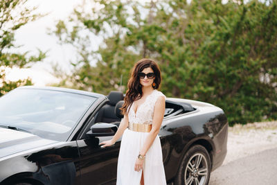 Portrait of young woman standing against car