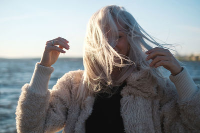 Woman with tousled hair standing against sea during sunset