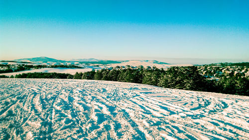 Snow covered field against clear blue sky