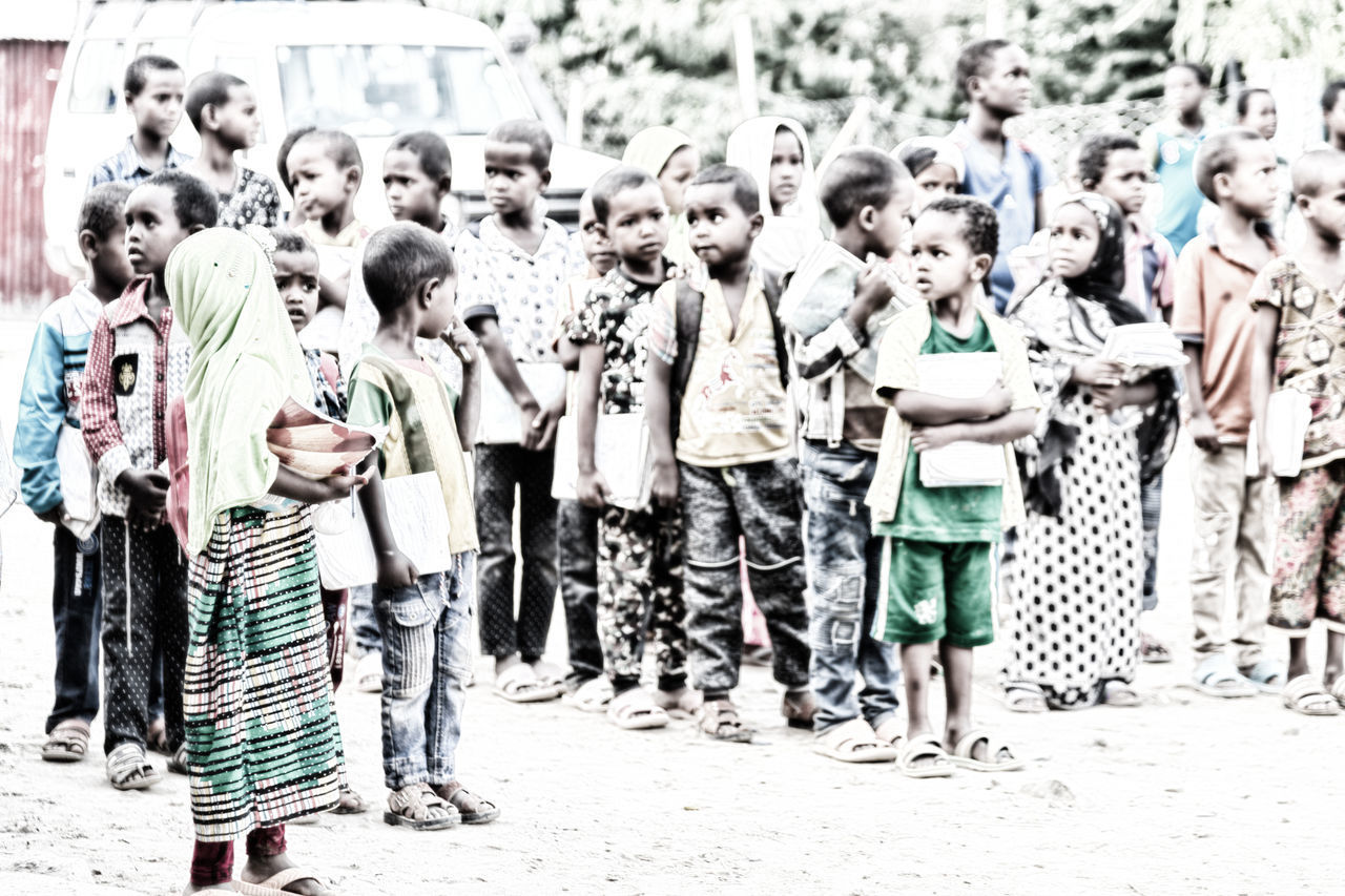 GROUP OF PEOPLE STANDING IN ROW AT MARKET STALL