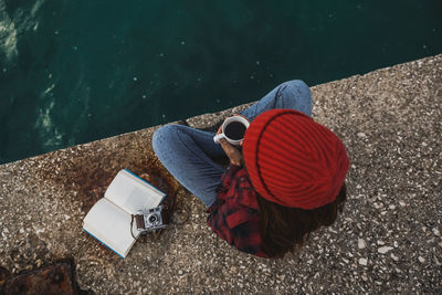 Directly above shot of woman with coffee sitting on pier by lake against sky