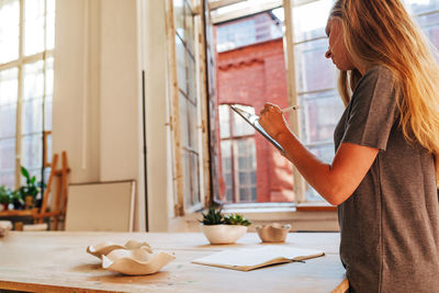 Side view of woman holding mobile phone while standing on table