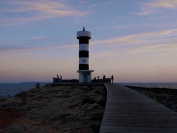 Lighthouse by sea against sky during sunset