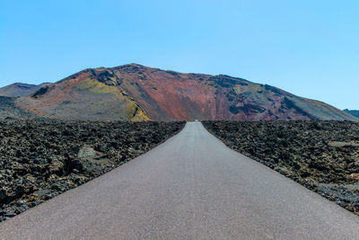 Road leading towards mountains against blue sky