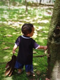 Rear view of boy standing by tree on land