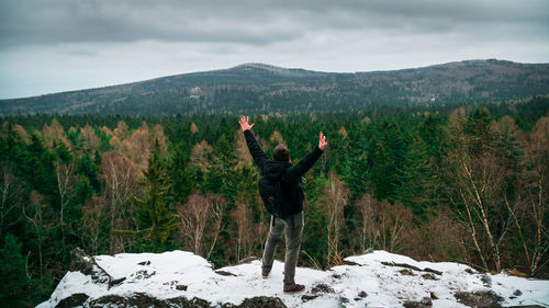 Rear view of man standing on snow covered cliff by trees during winter