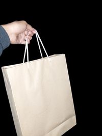 Cropped hand of woman holding bag against black background