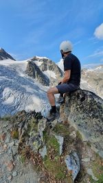 Side view of man sitting on mountains against sky