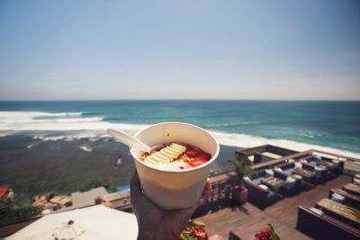 Close-up of person holding food against sea and clear sky