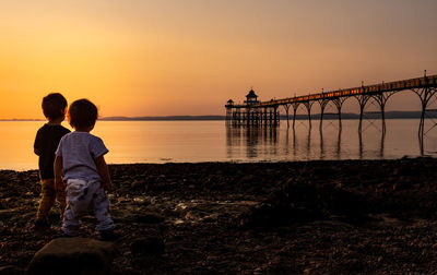 Rear view of children against sky during sunset with view of a pier