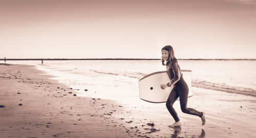 Portrait of girl carrying surfboard at beach during sunset