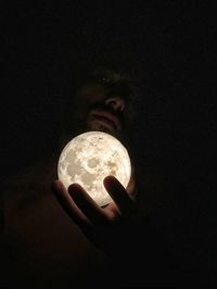 Close-up of hand holding illuminated light bulb in darkroom