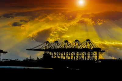 Silhouette cranes by sea against sky during sunset