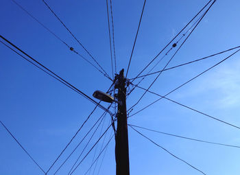 Low angle view of electricity pylon against blue sky