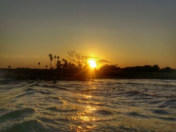 Scenic view of sea against bright sun at sunset