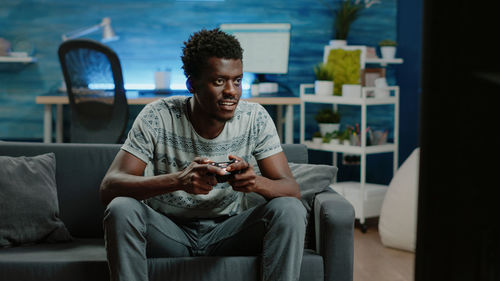 Man playing video game while sitting on sofa at home
