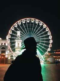 Rear view of silhouette people against illuminated ferris wheel at night