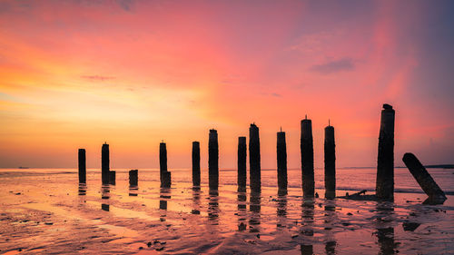 Wooden posts in sea against sky during sunset